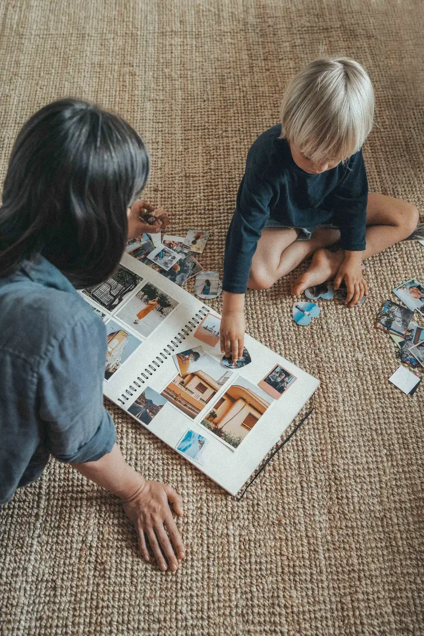 Mãe e filho sentados no chão montando um álbum, com fotos impressas espalhadas pelo tapete